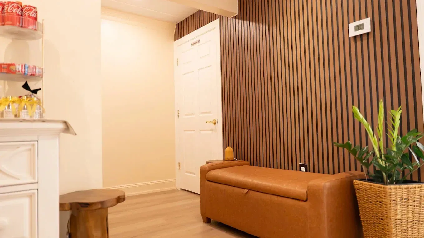 A warm-lit massage studio waiting lounge in the evening, low chairs set against a wood-slatted wall