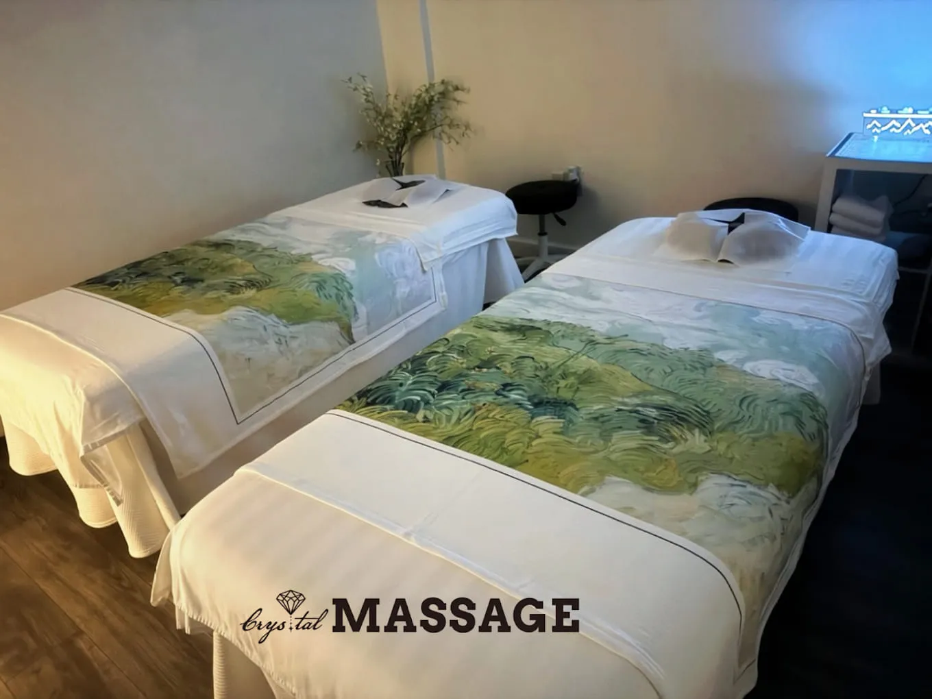 Second treatment room at Crystal Massage with two massage tables side by side, a stool between them and folded towels on a lit cart, Wichita, KS