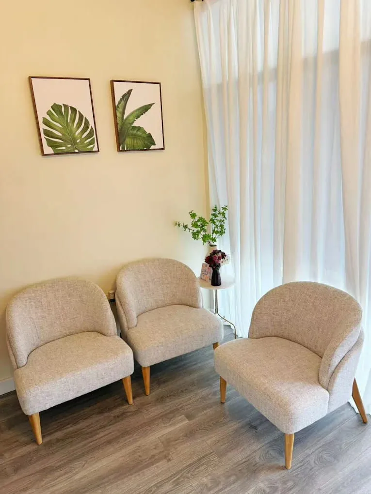 Waiting area with three woven armchairs, a sheer curtain over the window and two framed leaf prints at Crystal Massage, Wichita, KS