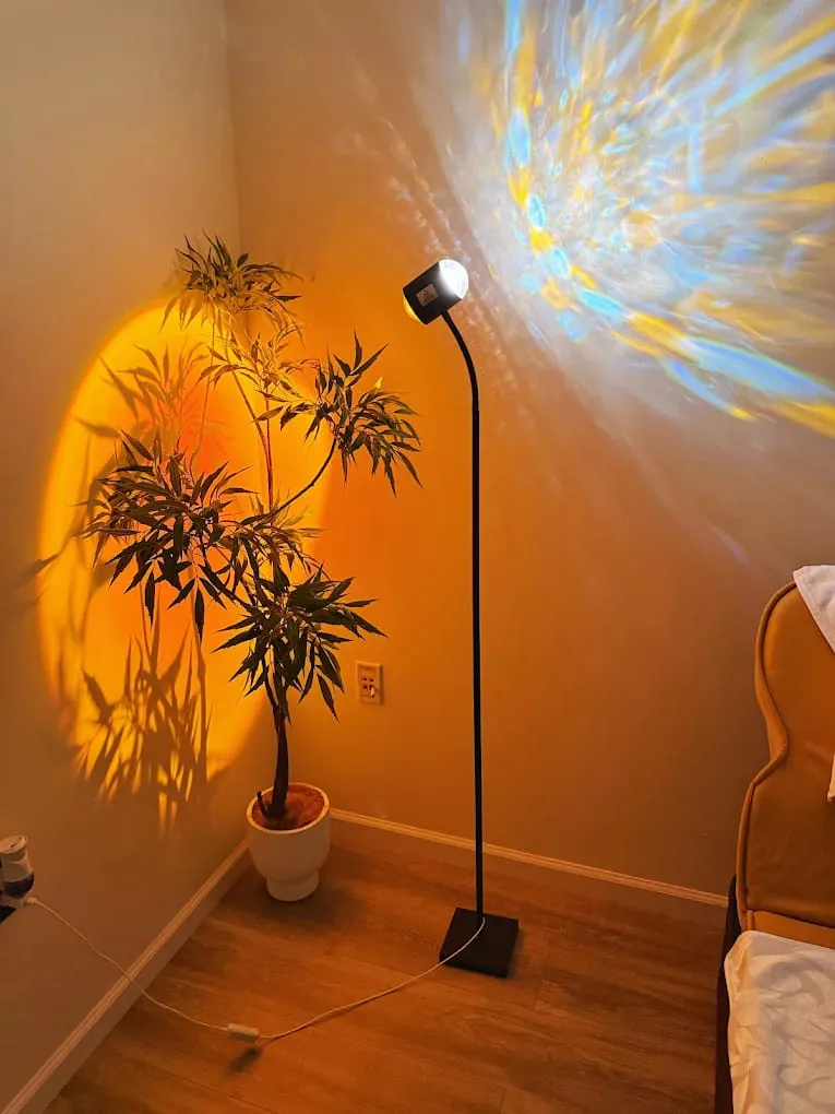 Floor lamp throwing an amber wash and a scatter of projected light across the wall behind a tall plant at Crystal Massage in Wichita, KS
